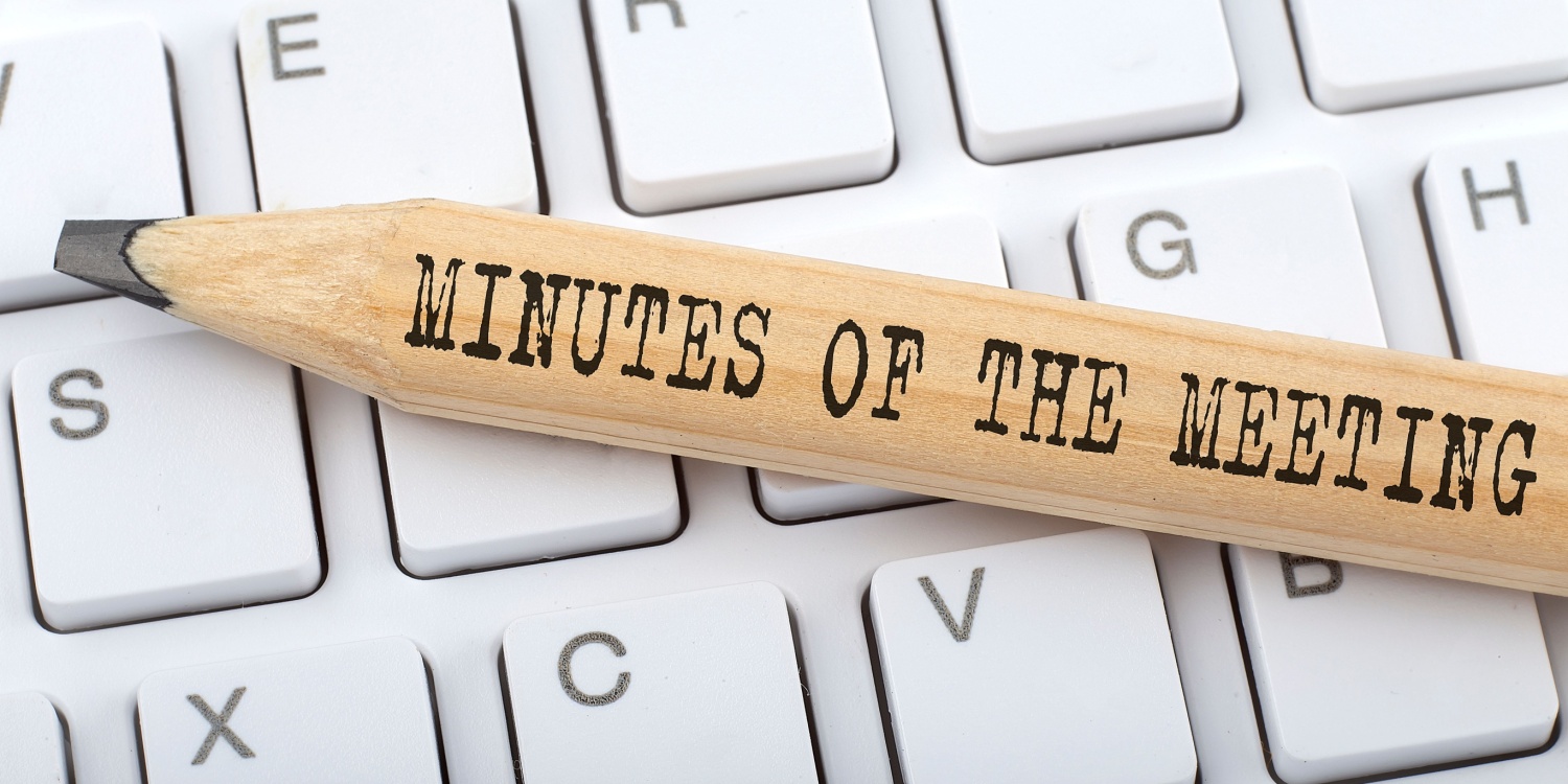 A pencil with text "minutes of the meeting" lying on a computer keyboard