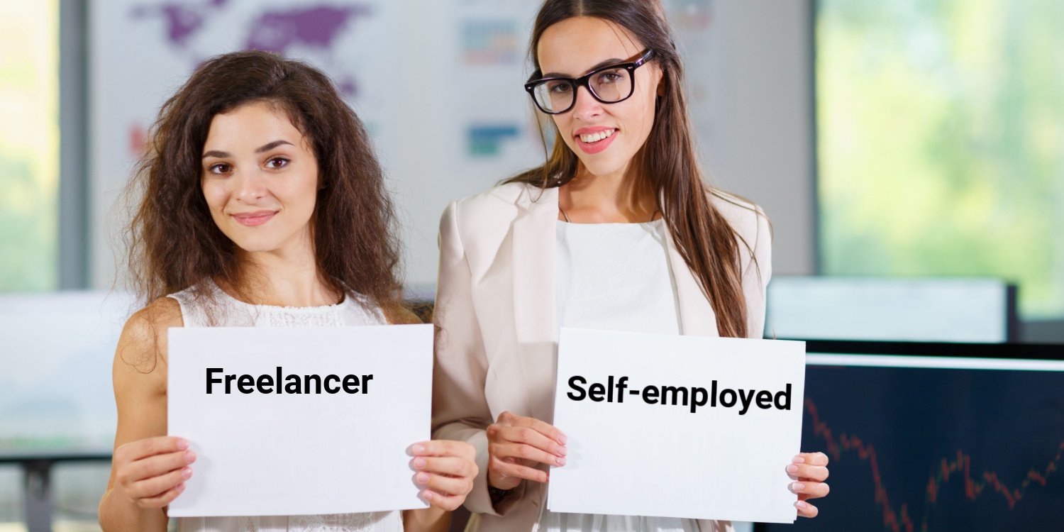 Two cheerful young business women holding up signs displaying the words 'freelancer' and 'self-employed.