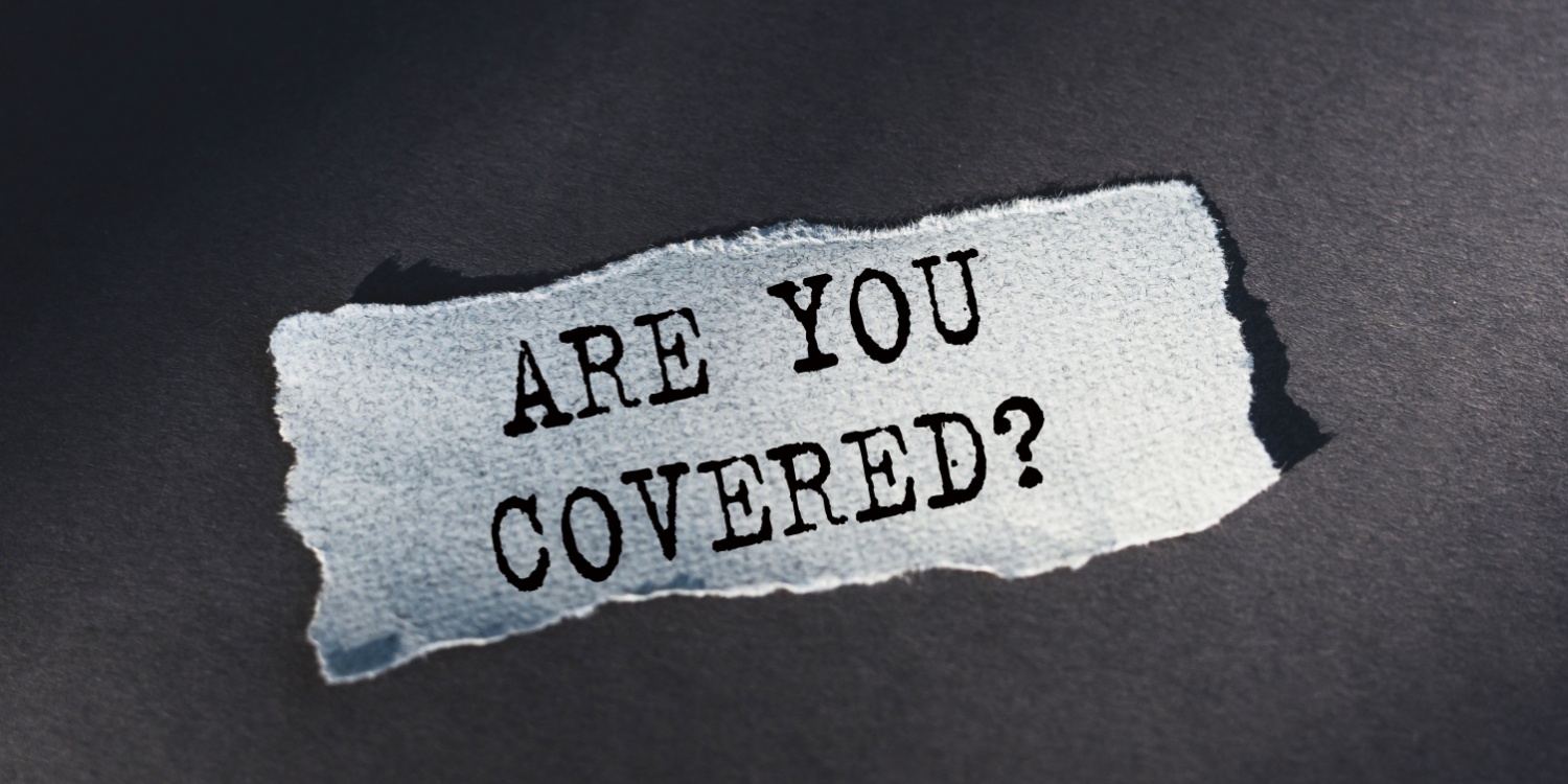 A torn piece of white paper lying on a dark grey background, and displaying the phrase 'ARE YOU COVERED?' printed in black font.