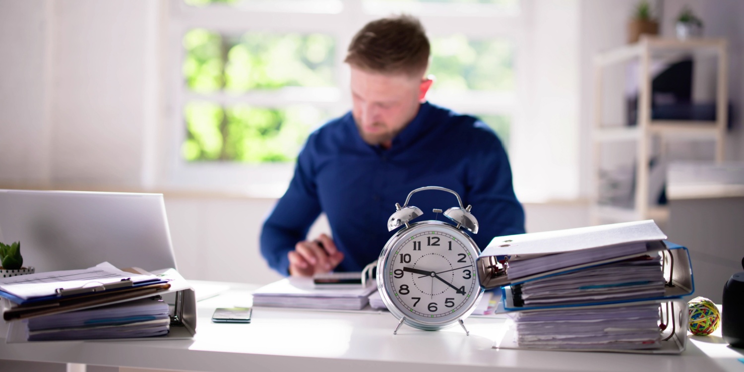 An accountant ponders a bill on his desk. There's an alarm clock to indicate the invoice is overdue and the firm paid late.