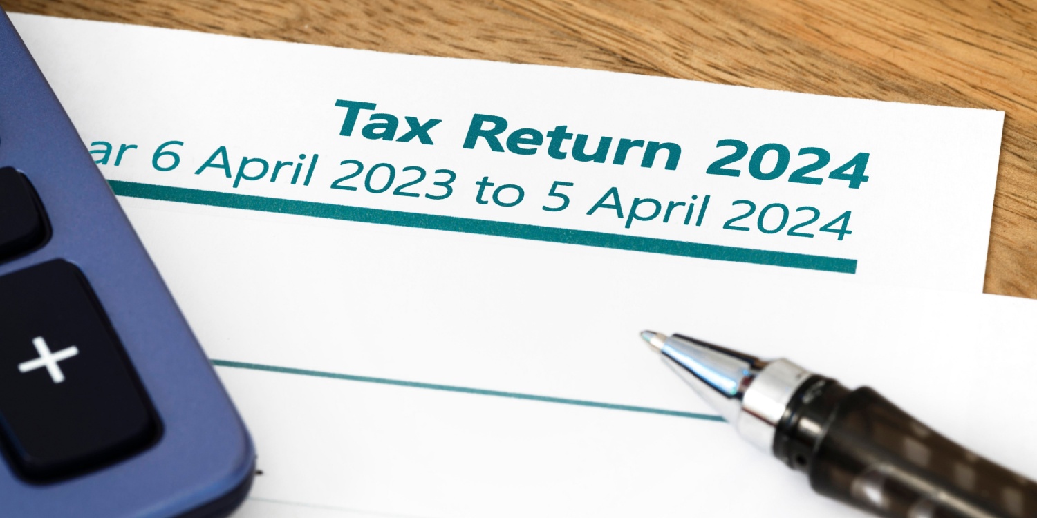 UK HMRC Self Assessment income tax return form 2024 lying on a wooden desk with a calculator and pen.